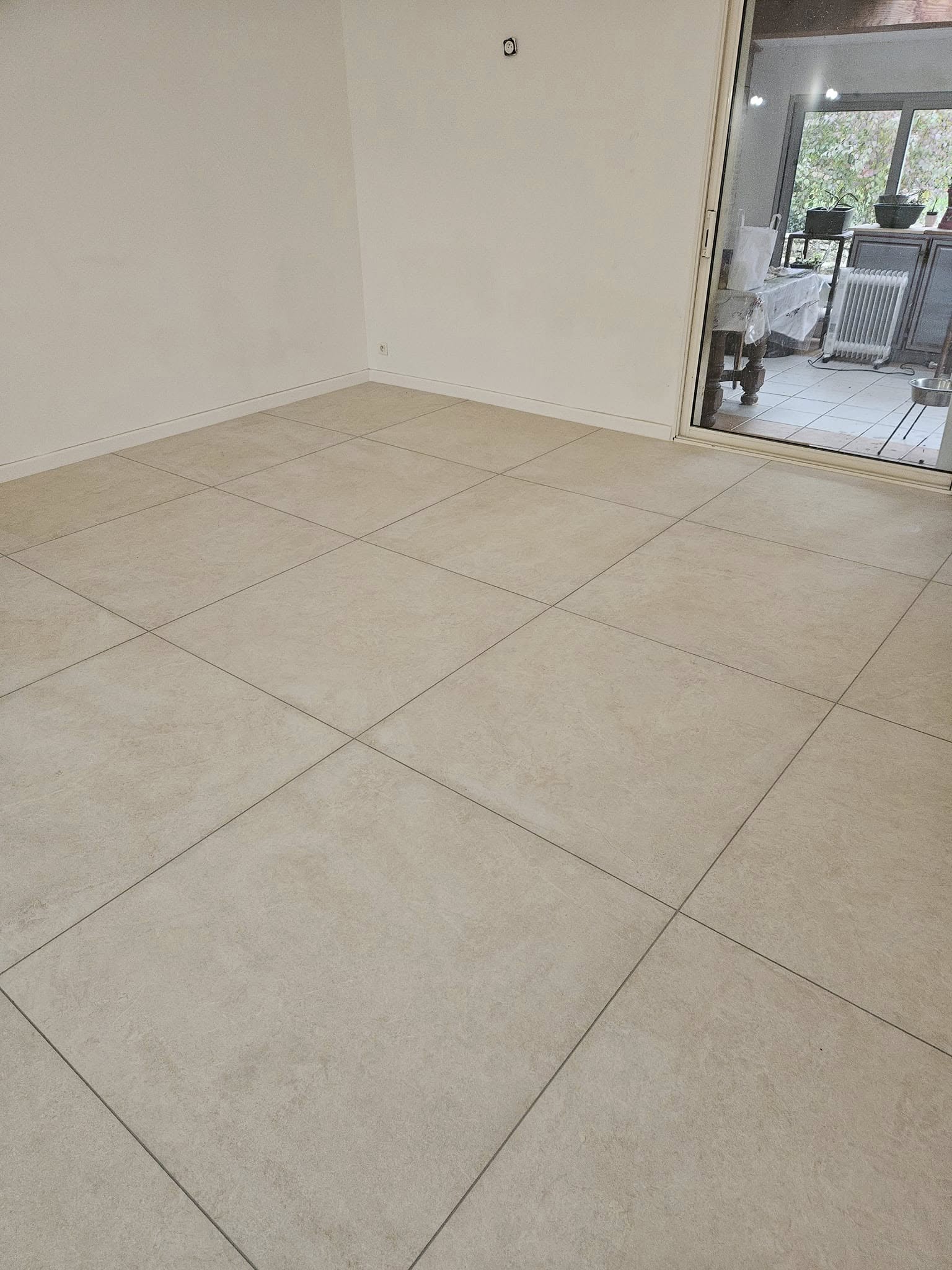 Finition d'un chantier de carrelage grand format 100 x 100 cm, avec joint gris clair sur l'ensemble de la surface.